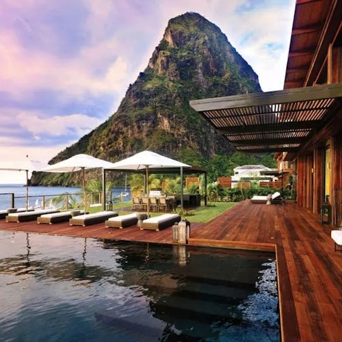 Luxury resort terrace with sun loungers overlooking tropical mountains and ocean at sunset.